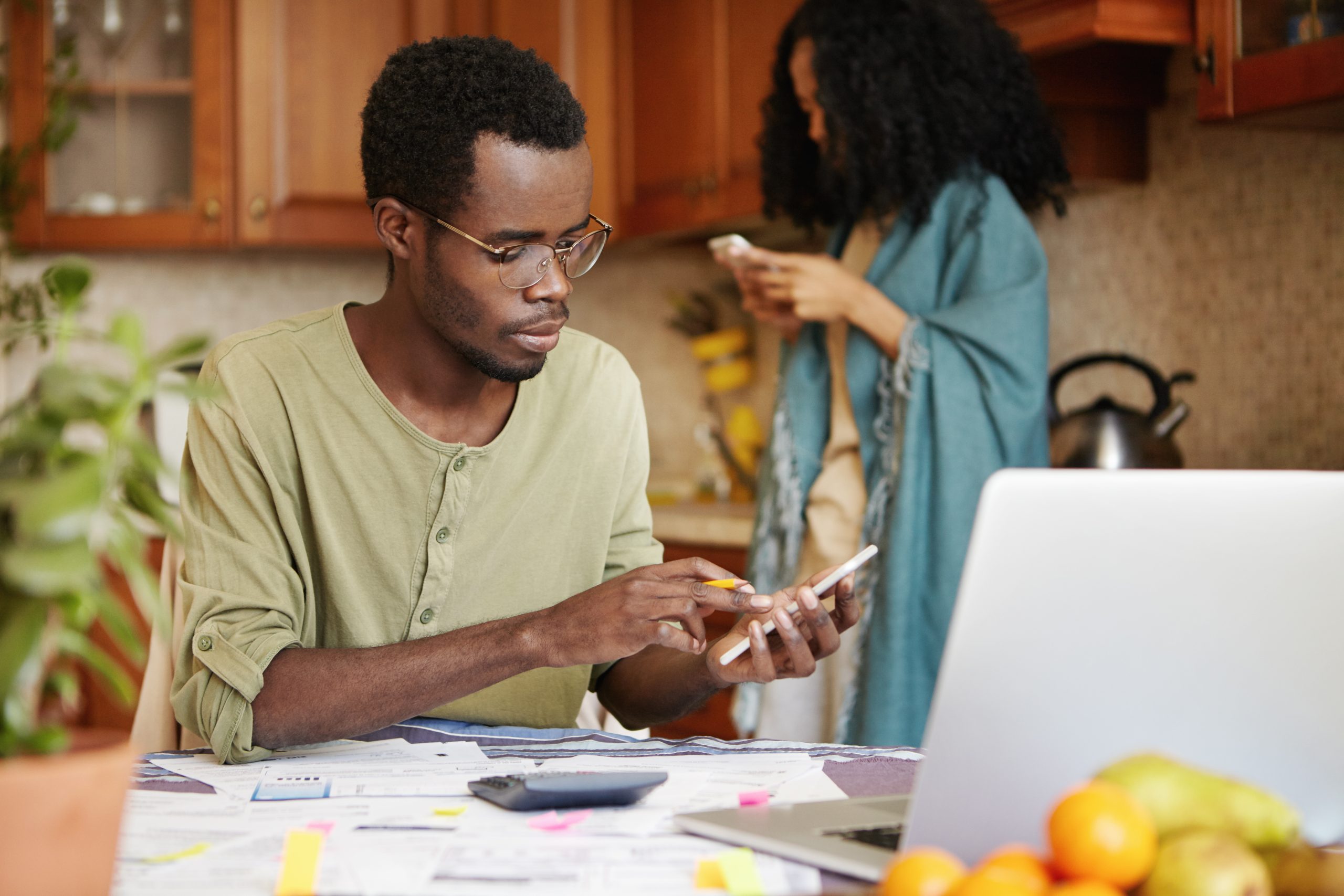 Business owner reviewing financial documents at a home desk with a smartphone, calculator, and laptop, symbolizing budget planning for Meta ads.