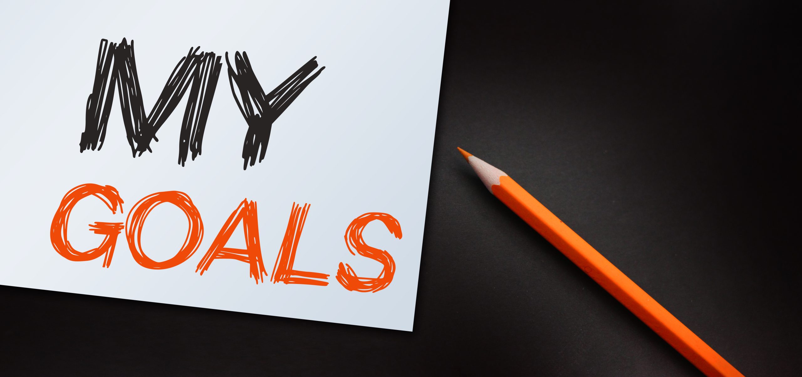 A sheet of paper labeled "MY GOALS" with bold, sketch-style lettering"MY" in black, "GOALS" in orange accompanied by an orange pencil resting on a dark surface. Symbolizes planning and intention, ideal for illustrating the first steps in starting a new Instagram account.